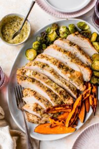 A beautifully roasted turkey breast surrounded by colorful vegetables on a sheet pan.