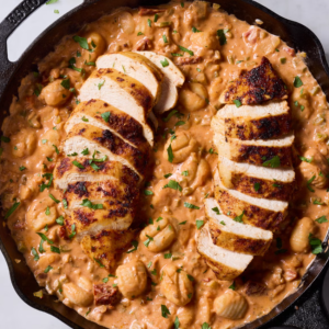 A skillet filled with Cajun-Spiced Chicken & Gnocchi, topped with fresh parsley and served in a creamy, golden sauce studded with vibrant vegetables and sun-dried tomatoes.