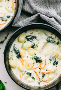 A warm bowl of creamy chicken gnocchi soup, garnished with fresh parsley and served with crusty bread